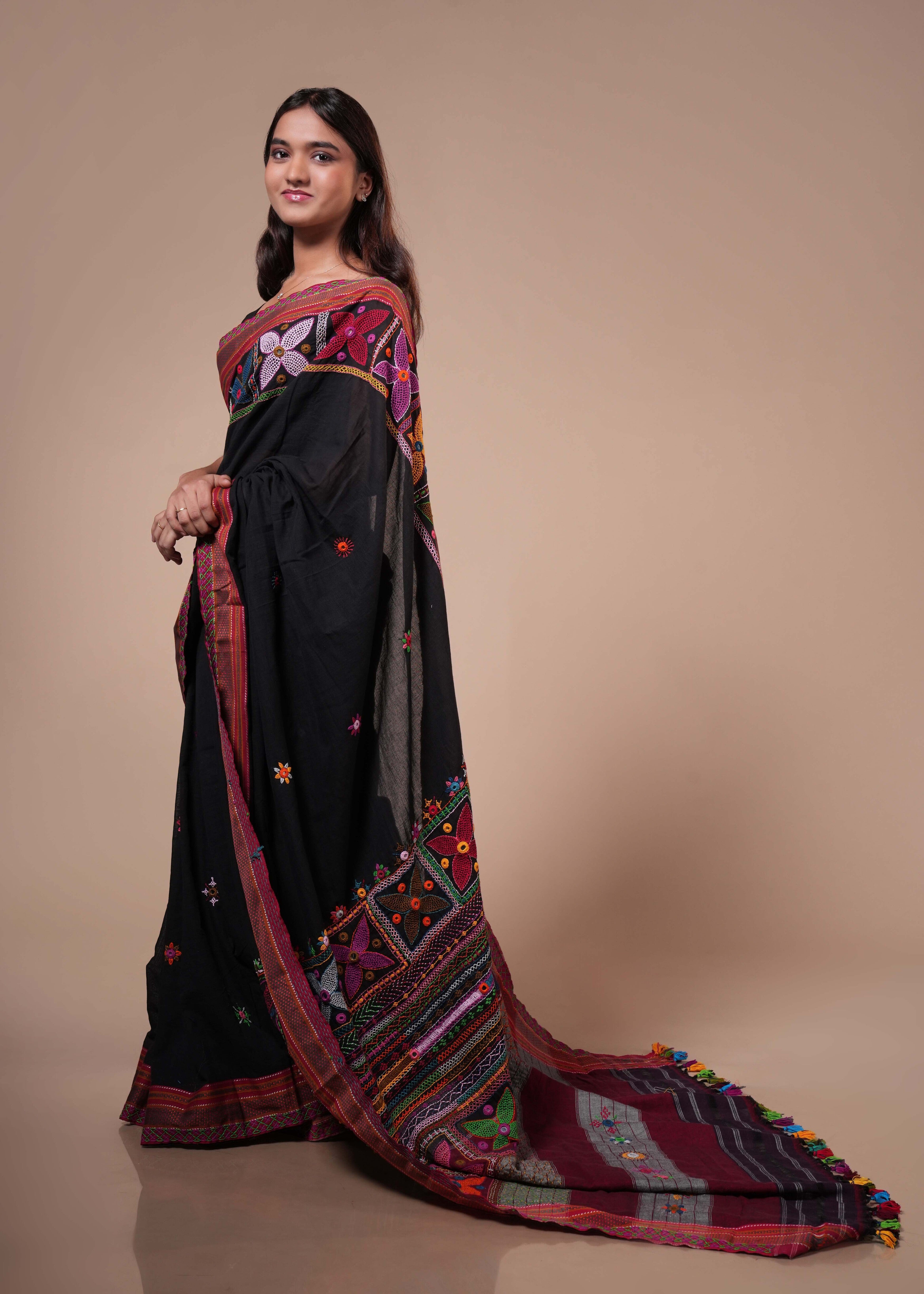 Woman wearing a black saree with colorful embroidery on a beige background